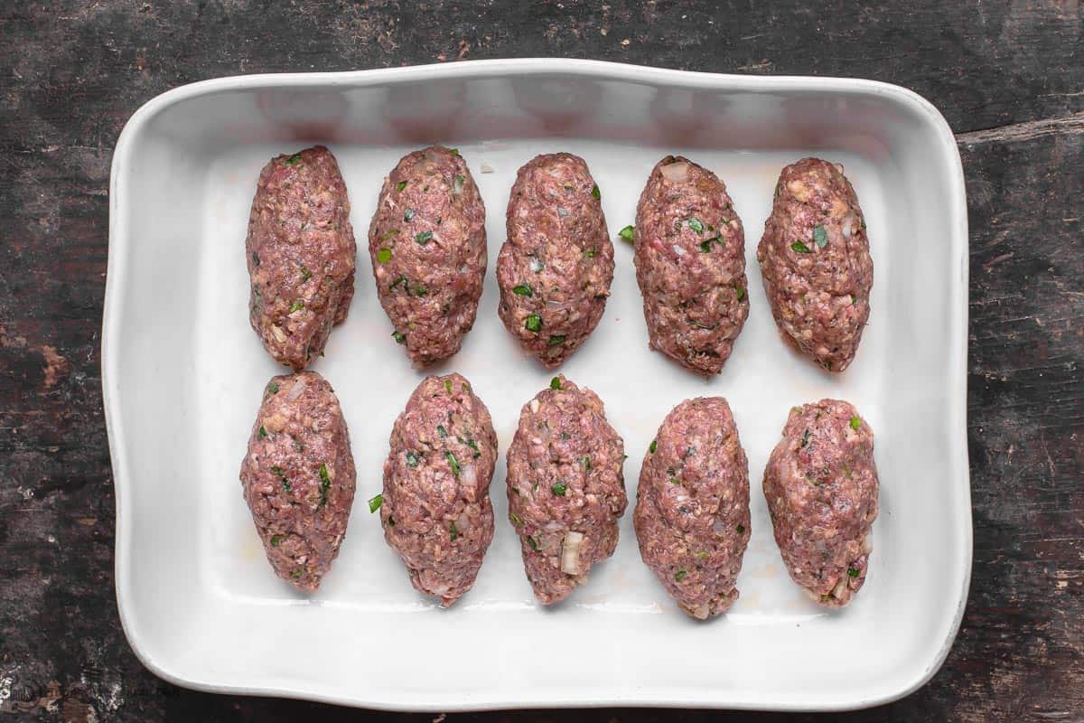 Meat mixture formed into elongated meatballs the shape of a football. Arranged in a baking dish