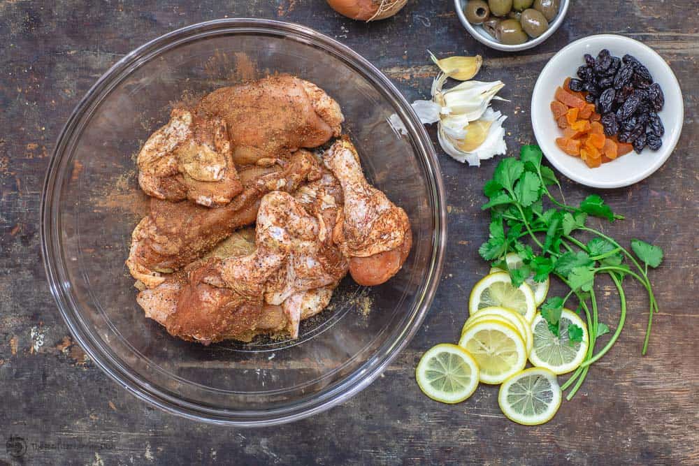 Chicken seasoned with Moroccan spice rub and left to marinate. Sliced lemons, cilantro, garlic, olives, dried fruit prepped on the side