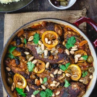 Moroccan chicken with lemons, olives, and dried fruit. Garnished with fresh cilantro and toasted almonds and served with couscous and more olives to the side