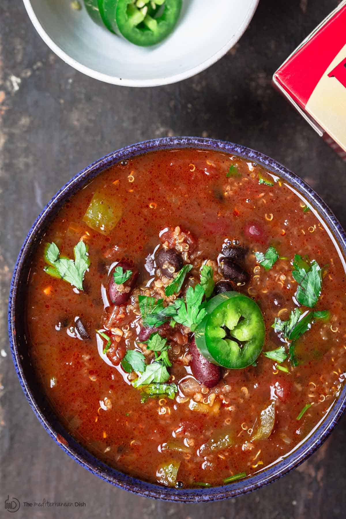 Bowl of Vegan Quinoa Chili with a side bowl of sliced jalapeno peppers