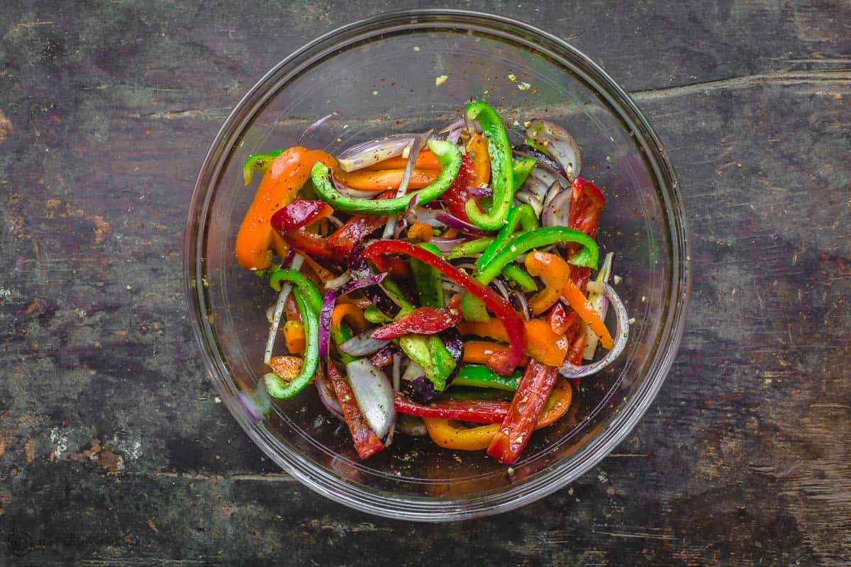 Thinly sliced bell peppers and red onions tossed in olive oil and spices in large mixing bowl