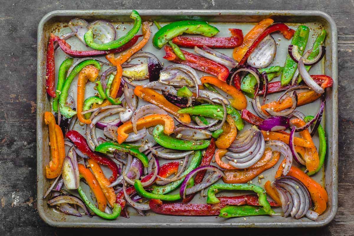 Bell peppers and red onion slices spread on sheet pan to bake