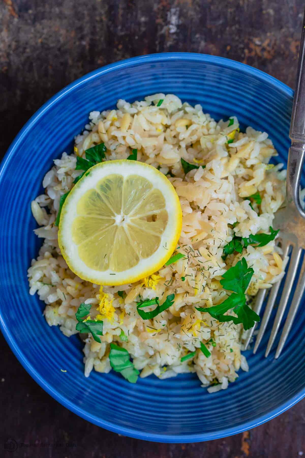 Greek lemon rice served on a blue plate with a fork. A lemon slice for garnish