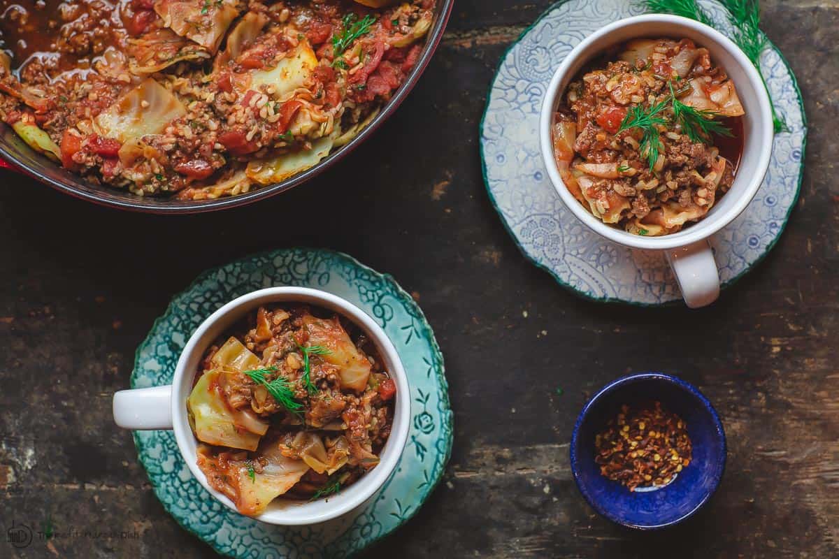 Unstuffed Cabbage Rolls served in bowls. Large pot and a small dish or hot pepper flakes on the side