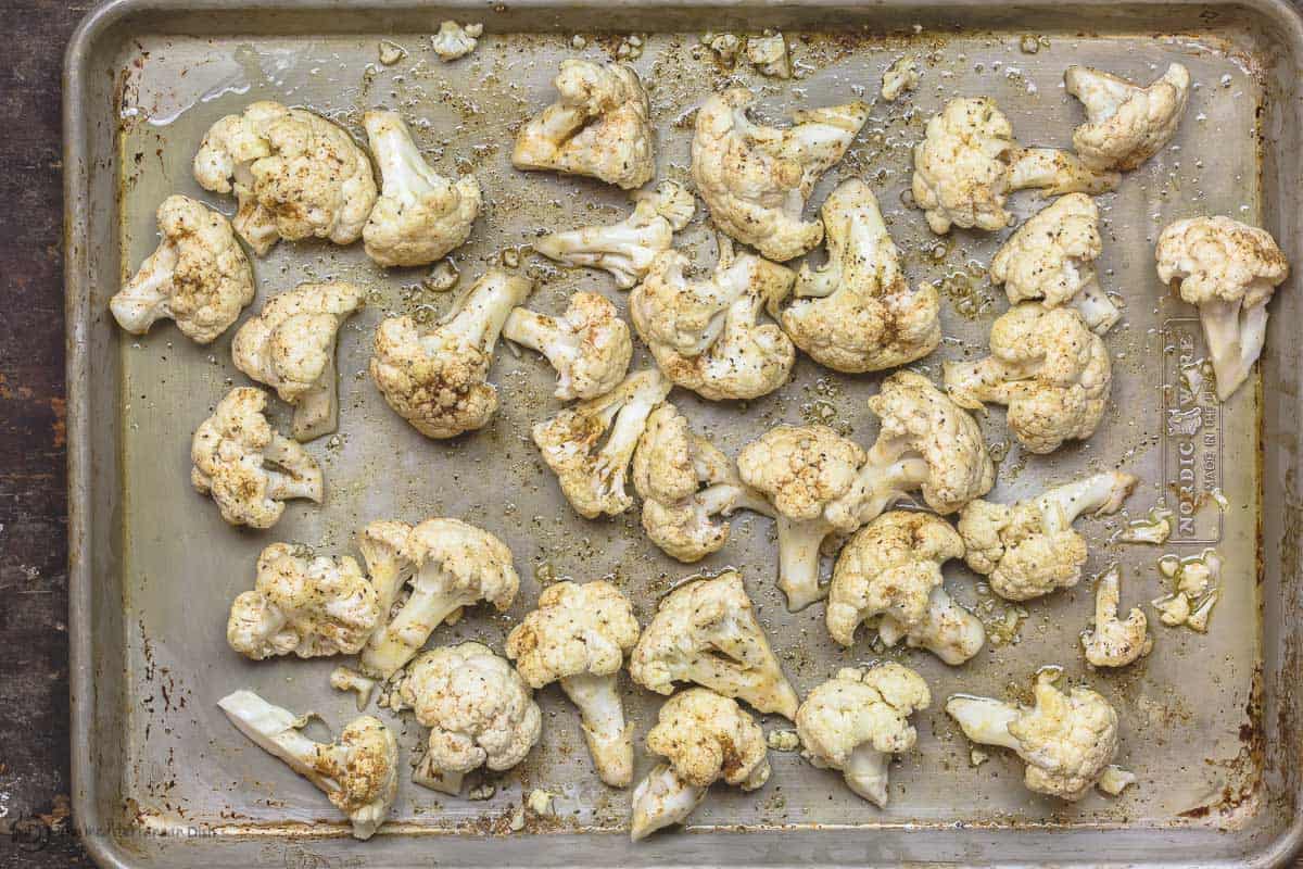 Cauliflower florets spread on baking sheet and seasoned with cumin and harissa spice. Drizzled with olive oil. 