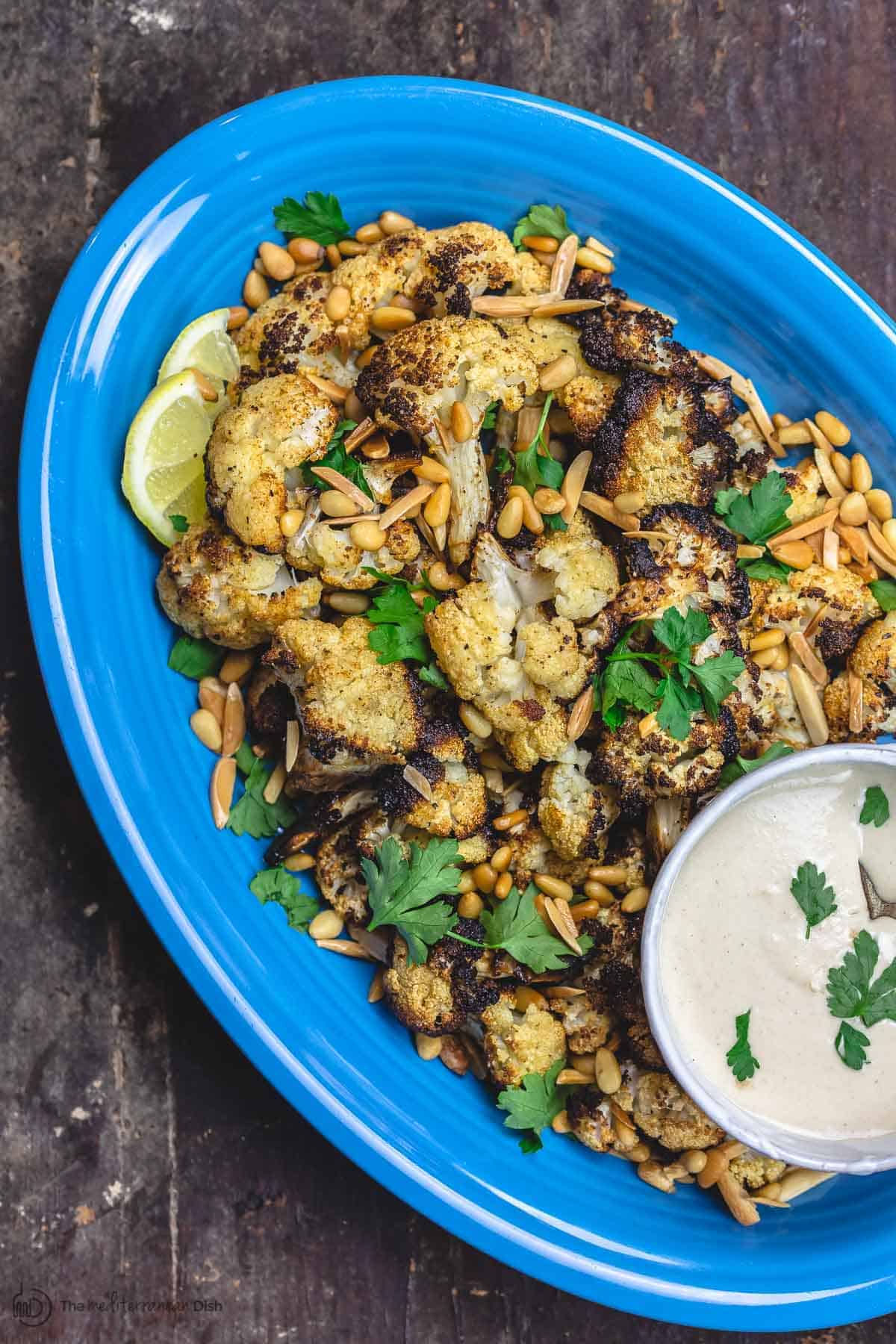 Best Roasted Cauliflower with cumin and lemon. Served on a large platter and garnished with toasted nuts, and parsley. A side of tahini sauce for dipping