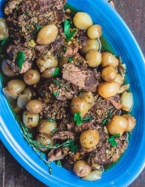 Slow Cooker Boneless Leg of Lamb Served on Platter atop of a Bed of Pearl Onions. Parsley garnish