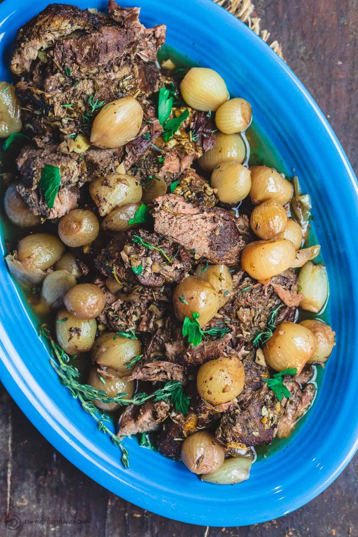 Slow Cooker Boneless Leg of Lamb Served on Platter atop of a Bed of Pearl Onions. Parsley garnish