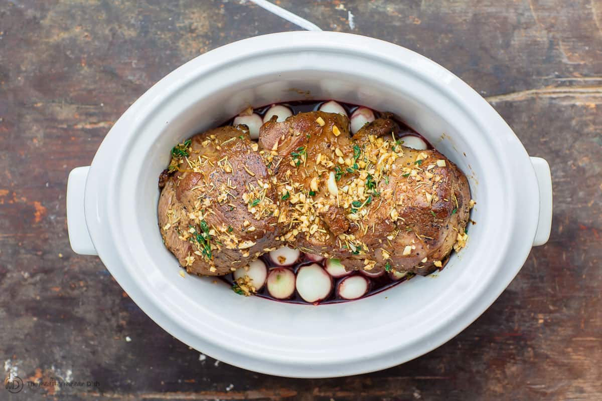 Boneless leg of lamb added on top of pearl onions in slow cooker with wine and broth