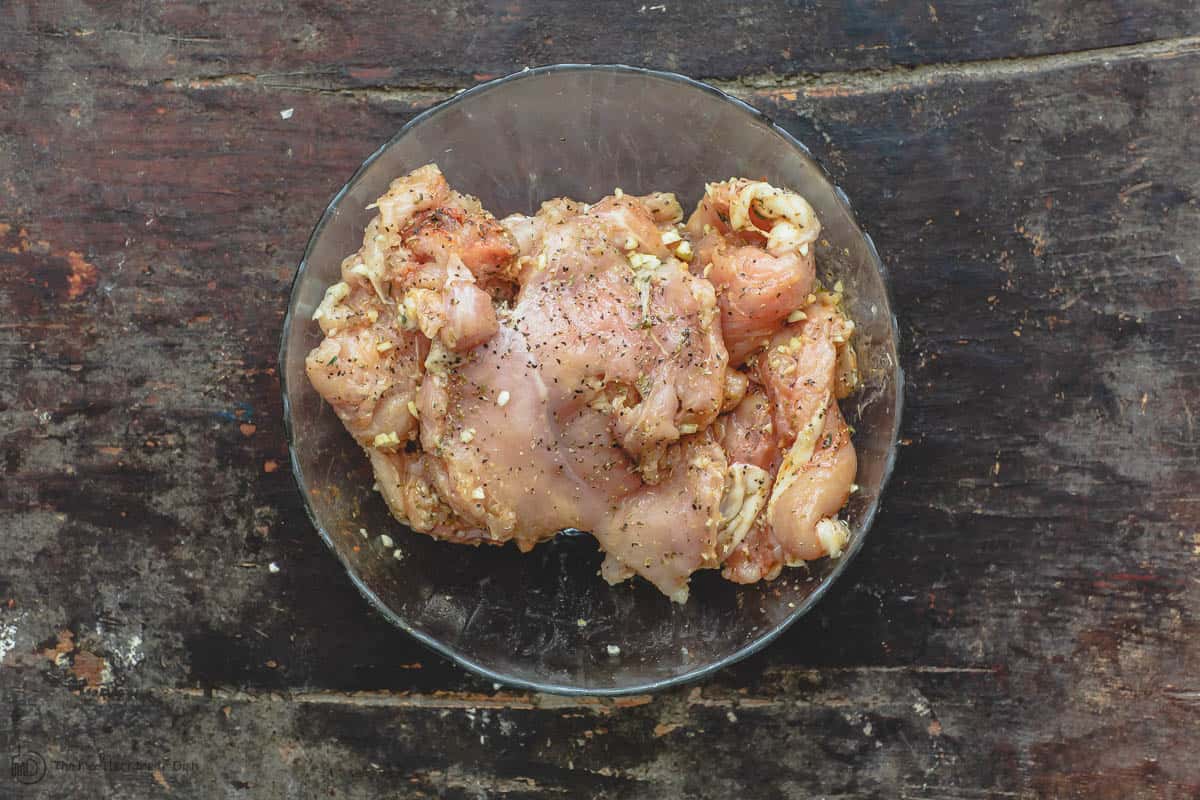 Chicken breast combined with spices, fresh garlic, olive oil and lemon juice in mixing bowl