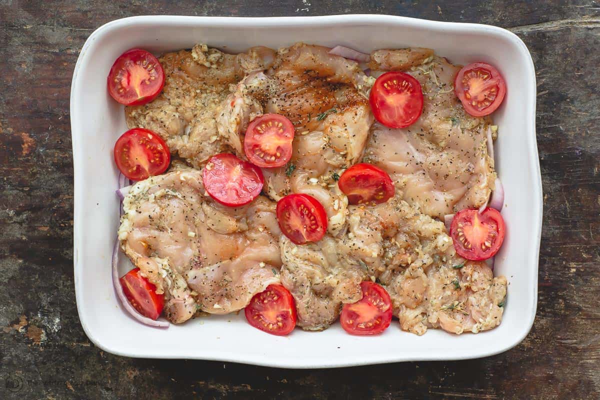 Chicken breasts arranged in a baking dish with red onions and tomatoes. Ready for baking