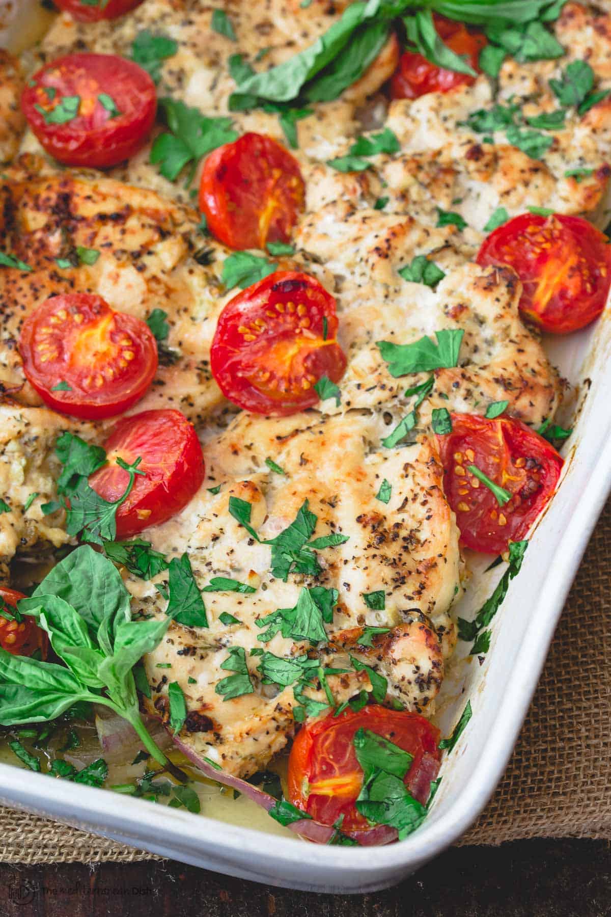 Italian baked chicken in baking dish, garnished with parsley and basil. 