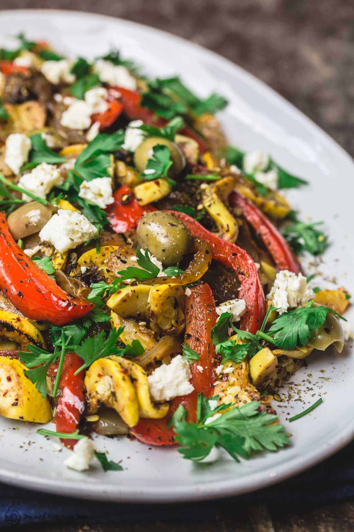 Mediterranean sauteed yellow squash on serving platter with garnish of feta, parsley, and olives