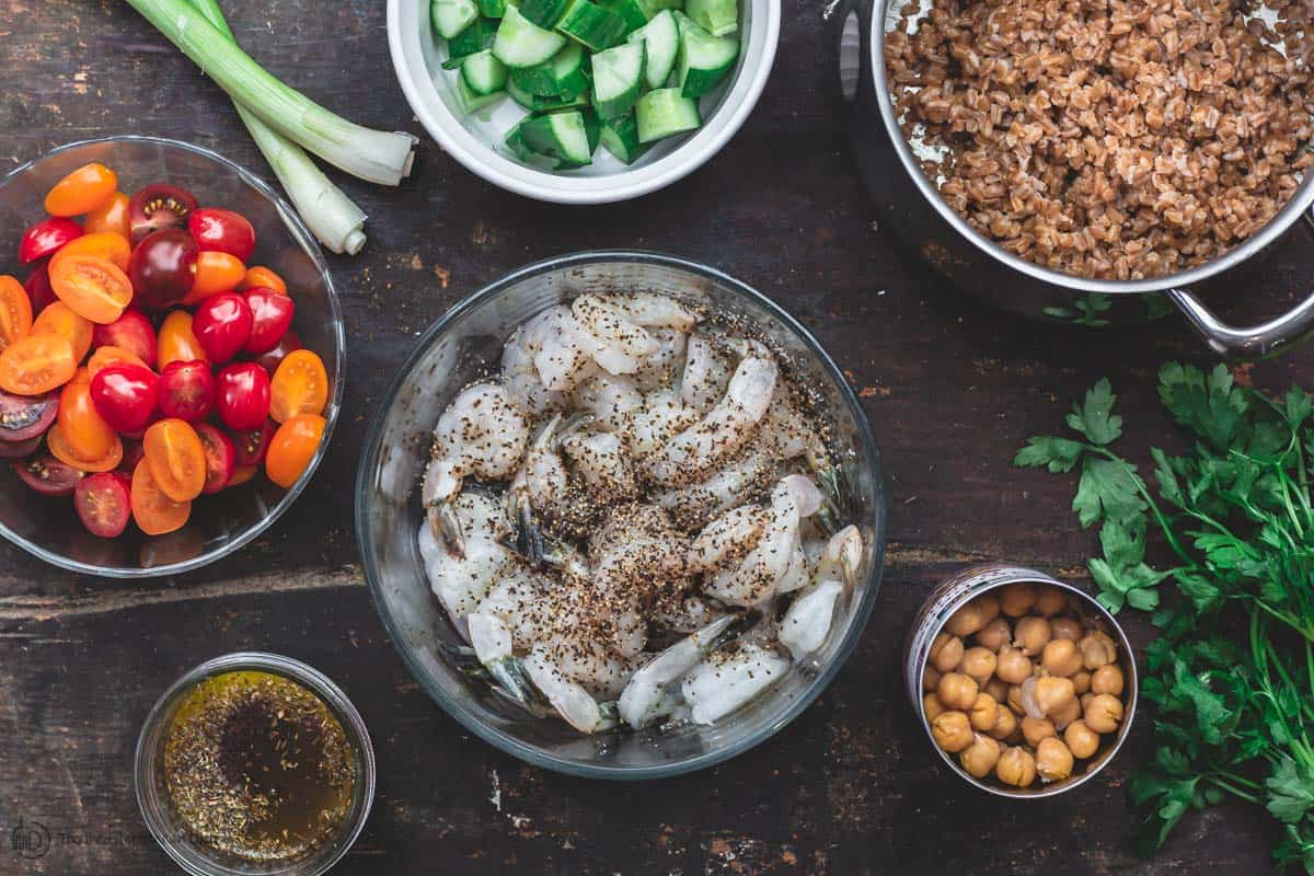 Ingredients for farro salad including cherry tomatoes, chickpeas, cooked farro, cucumbers and fresh herbs