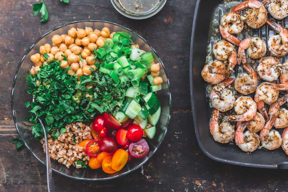 Farro salad ingredients in a bowl. Side of cooked shrimp