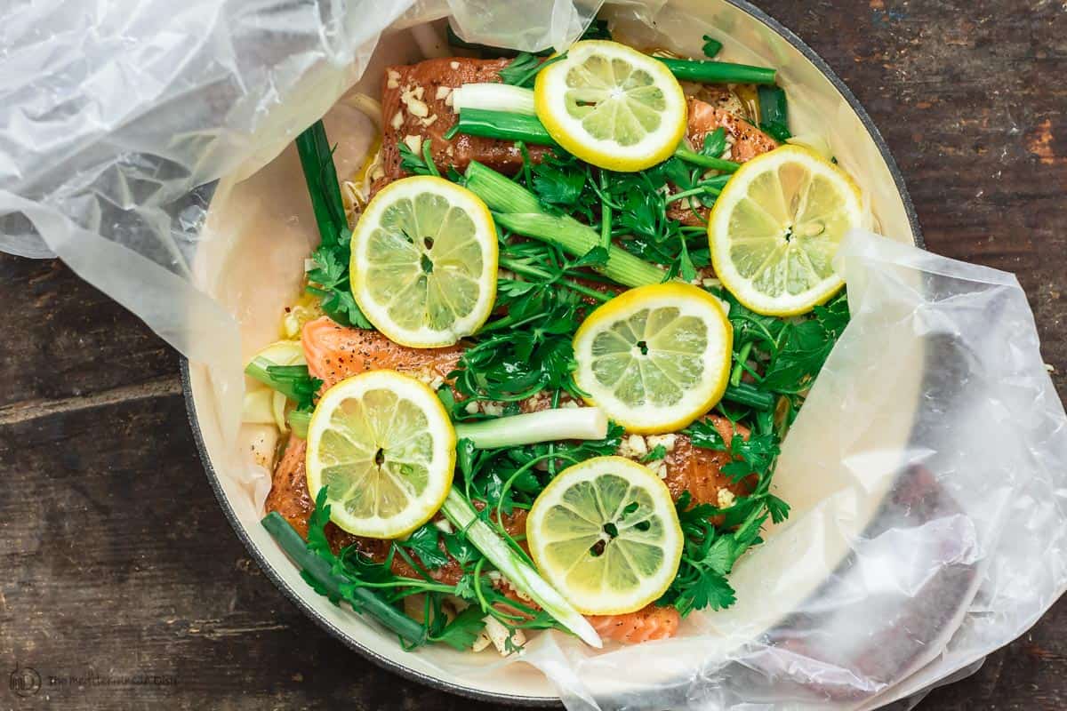Lemon slices arranged over salmon and fresh herbs. White wine poured over.