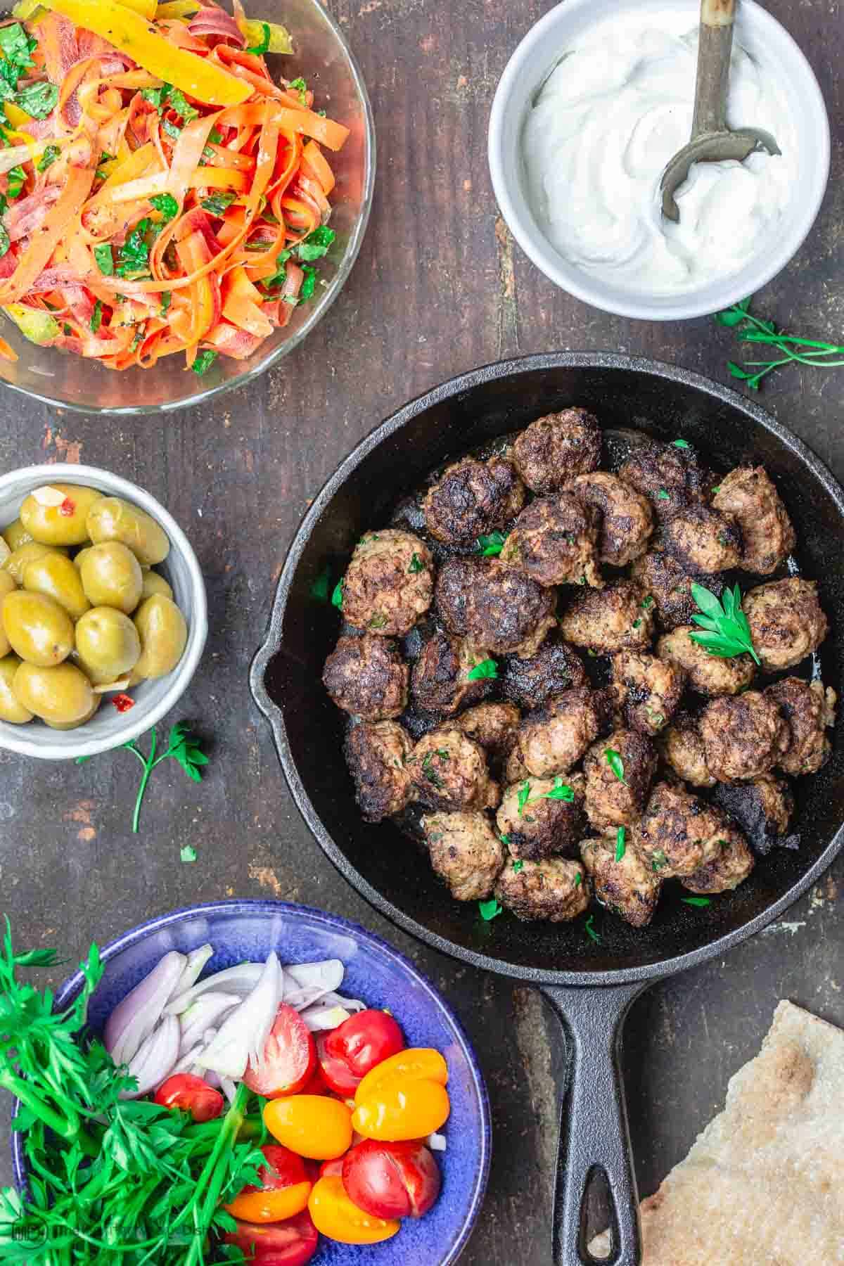 Large spread with Morrocan Meatballs and different sides including Tztaziki Sauce, Olives, Carrot Salad, Pita Bread