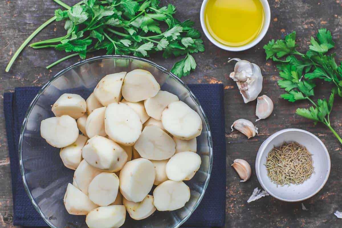 Ingredients for boiled potatoes, including potatoes, fresh parsley, garlic, rosemary and olive oil