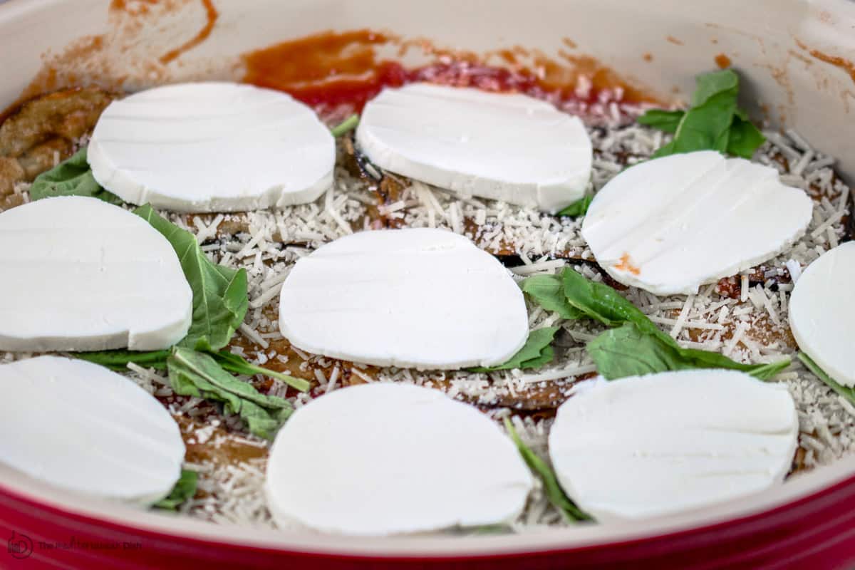 Another layer of mozzarella slices arranged on top of slices of eggplant, Parmesan, and fresh basil leaves