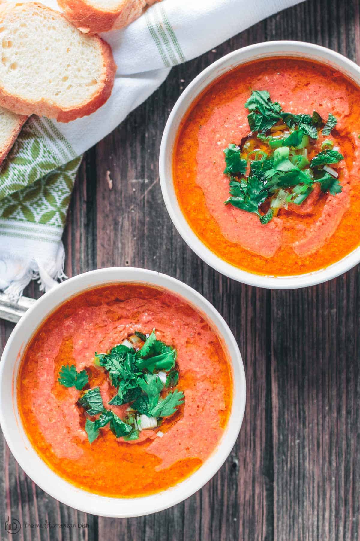 Gazpacho in bowls, garnished with fresh herbs and a generous drizzle of olive oil. A side of bread