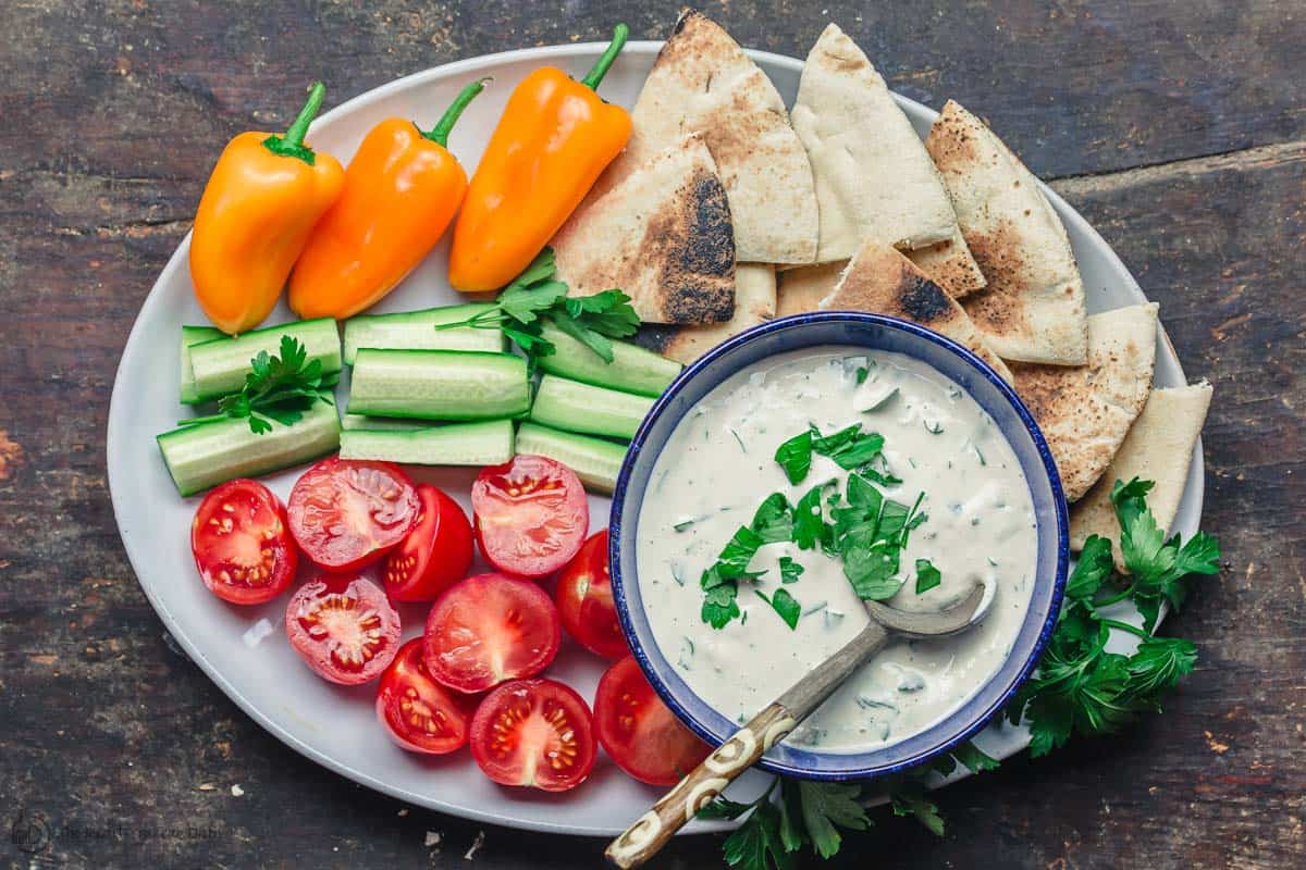 Tahini sauce with fresh vegetables and a side of pita wedges