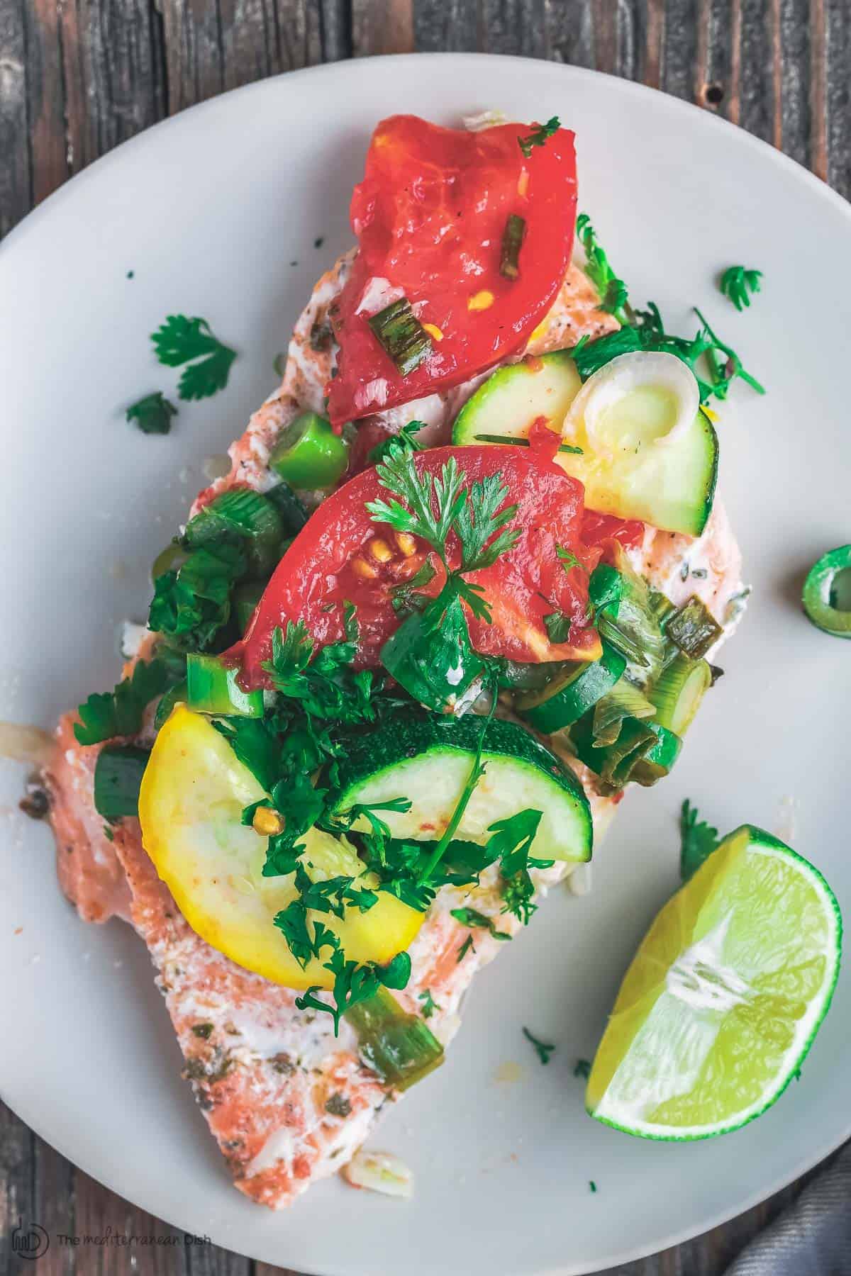 Oven baked salmon served on a plate with vegetables and parsley