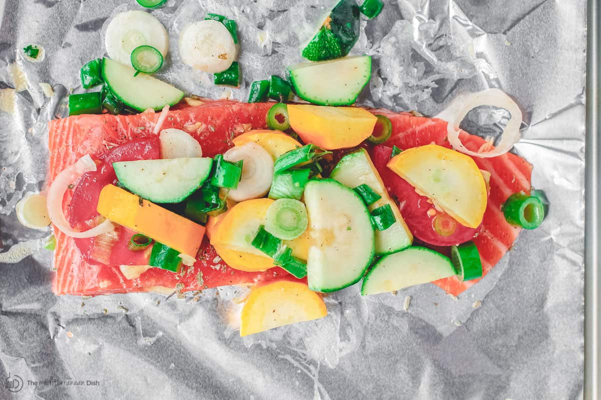 Sliced vegetables laid on top of salmon fillet in foil