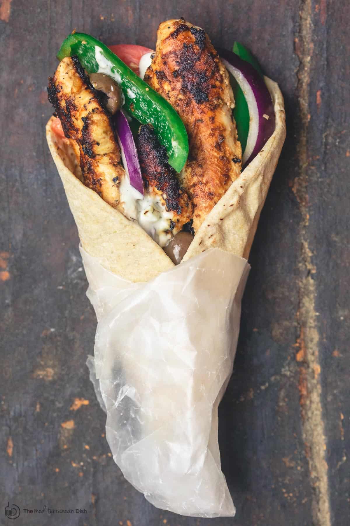 A chicken gyro wrap with tomatoes, onions, green peppers and olives