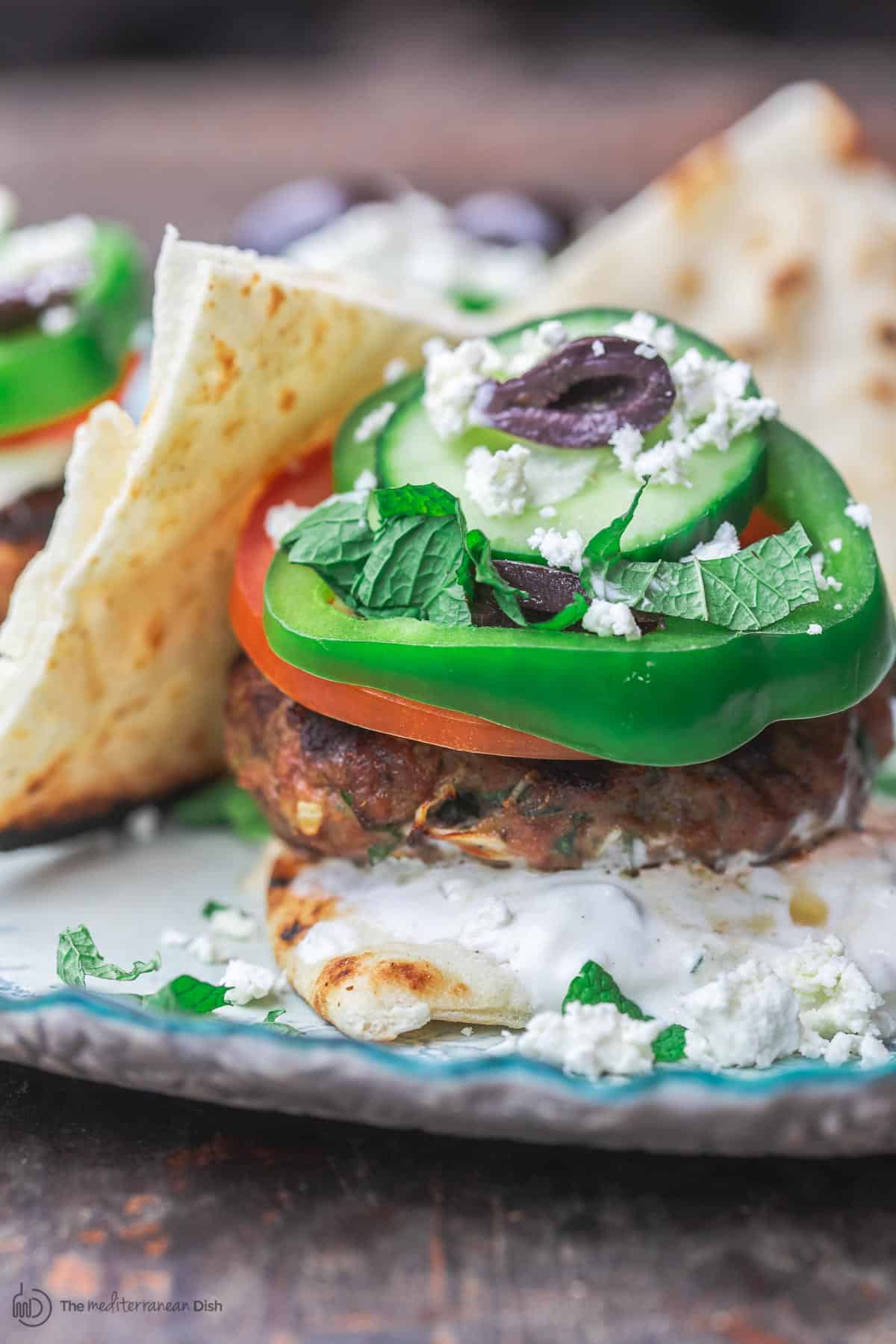 Greek lamb burgers with tzatziki sauce, green peppers, cucumbers, tomatoes, olives and feta cheese on a flat bread