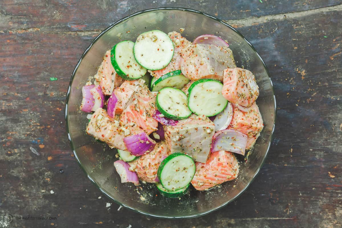 Salmon cutlets with slices of zucchini and red onion, marinated in a mixing bowl