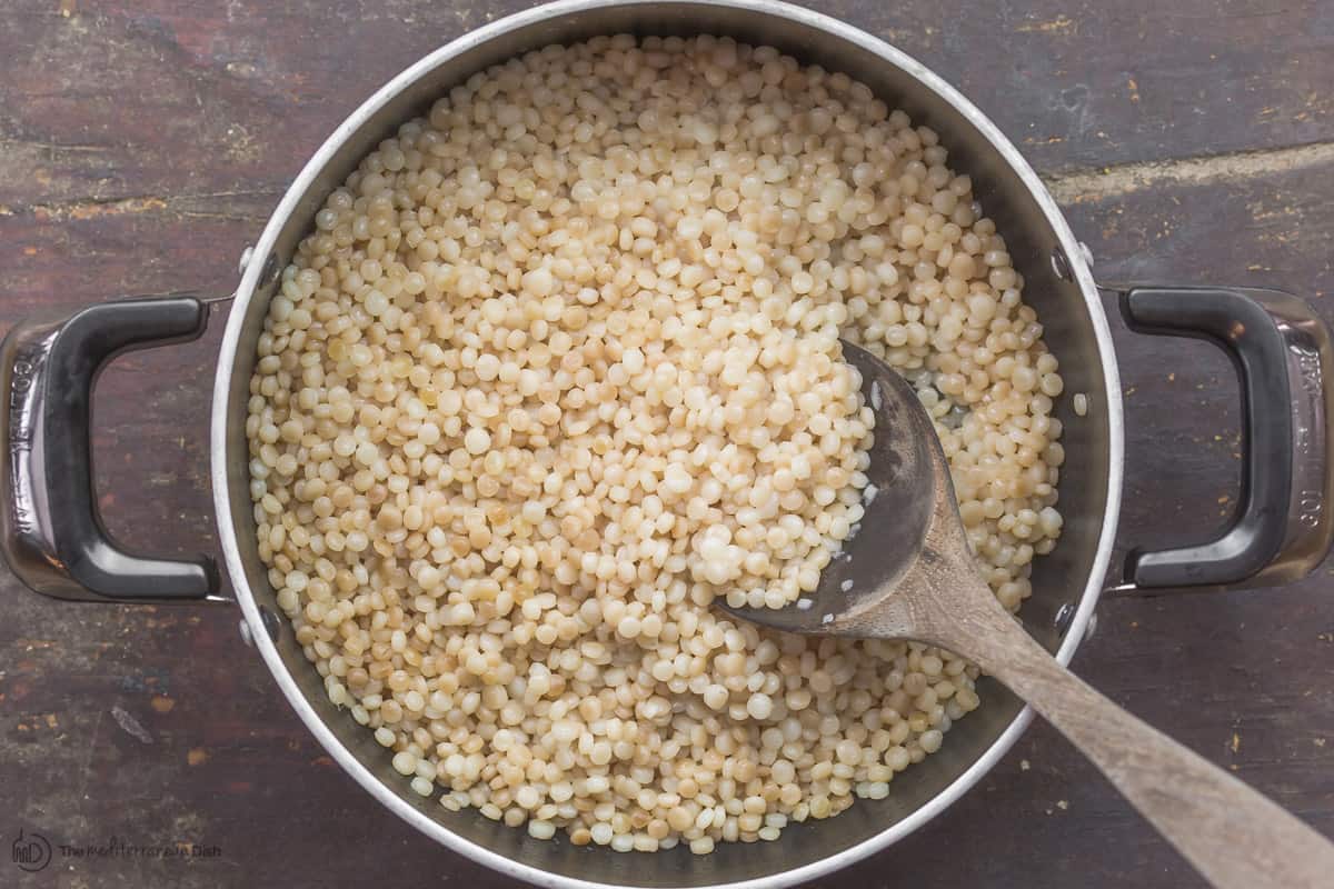 Cooked pearl couscous in a pot with large serving spoon