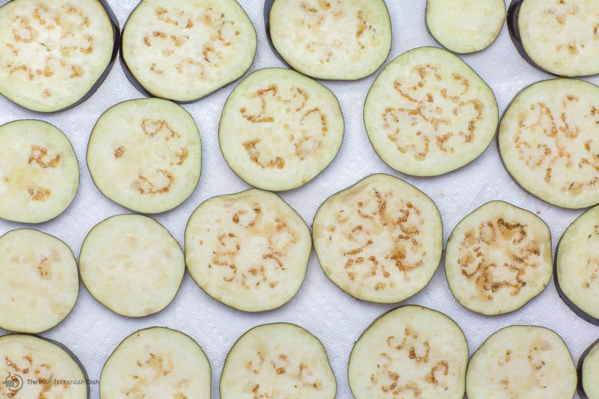 Raw eggplant slices, salted and spread on a paper-towel lined tray