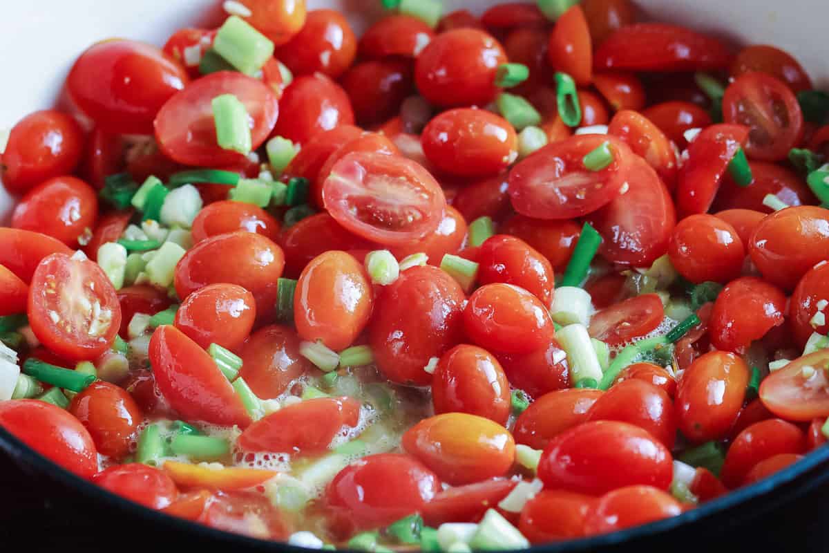 Roma tomatoes and diced green onions fried in a large pan