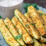 Baked zucchini sticks, stacked on a plate with a side of Tzatziki sauce