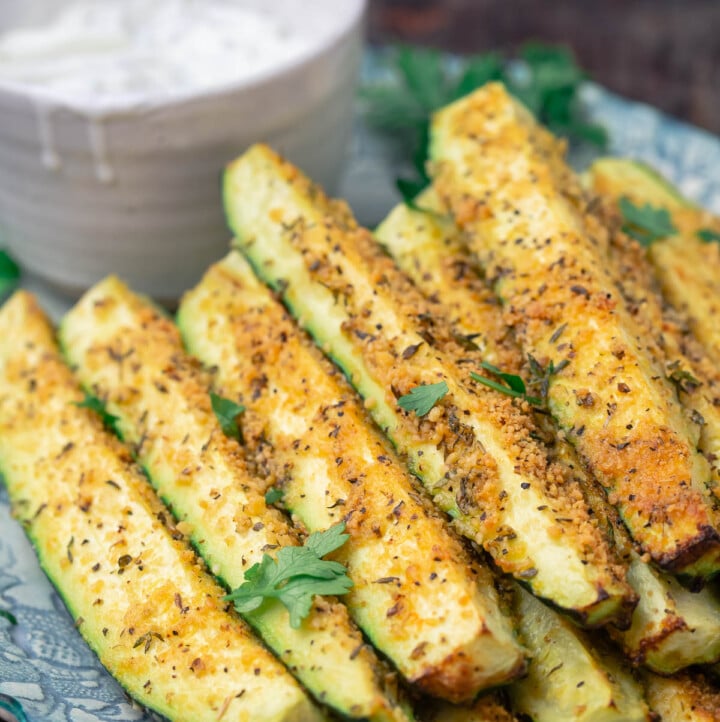 Baked zucchini sticks, stacked on a plate with a side of Tzatziki sauce
