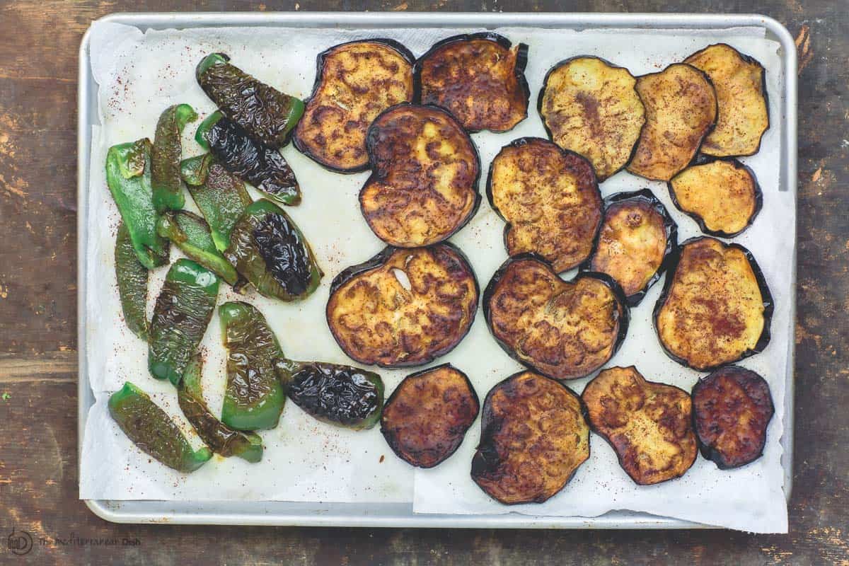 Slices of fried eggplant and green peppers on a baking sheet with parchment paper