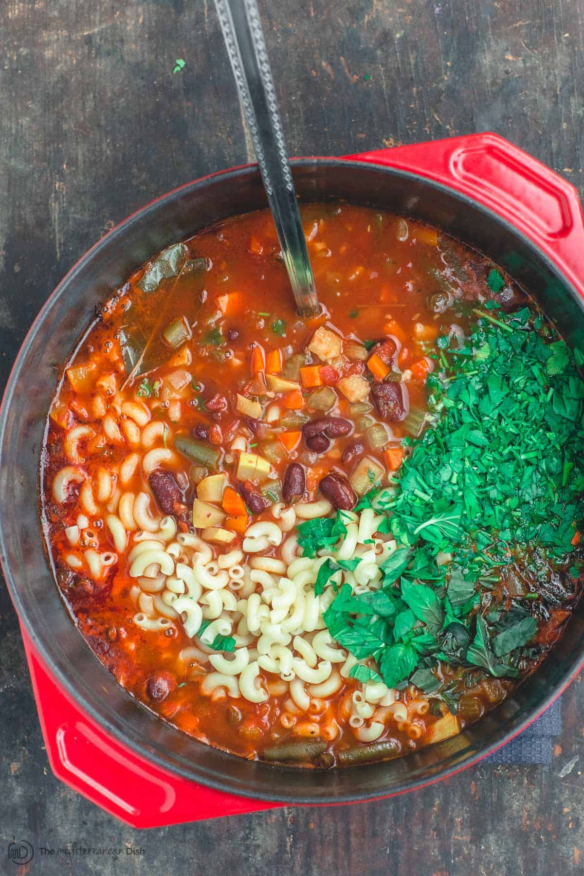 Minestrone soup in a large pot with herbs and vegetables.