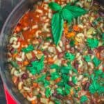 Minestrone soup in a pot with herbs and vegetables.