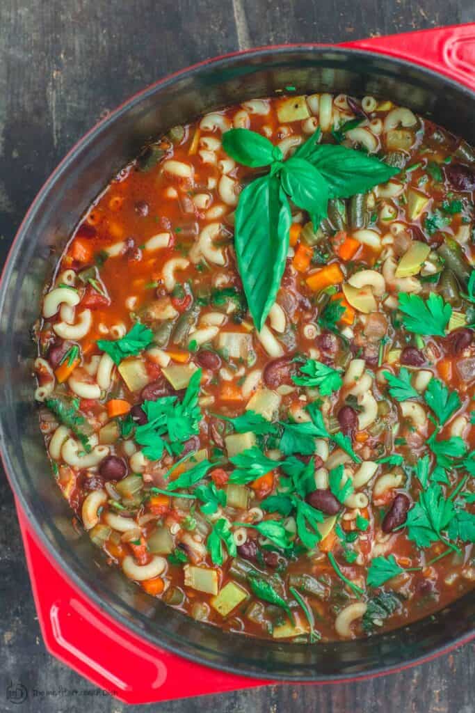 Minestrone soup in a pot with herbs and vegetables.