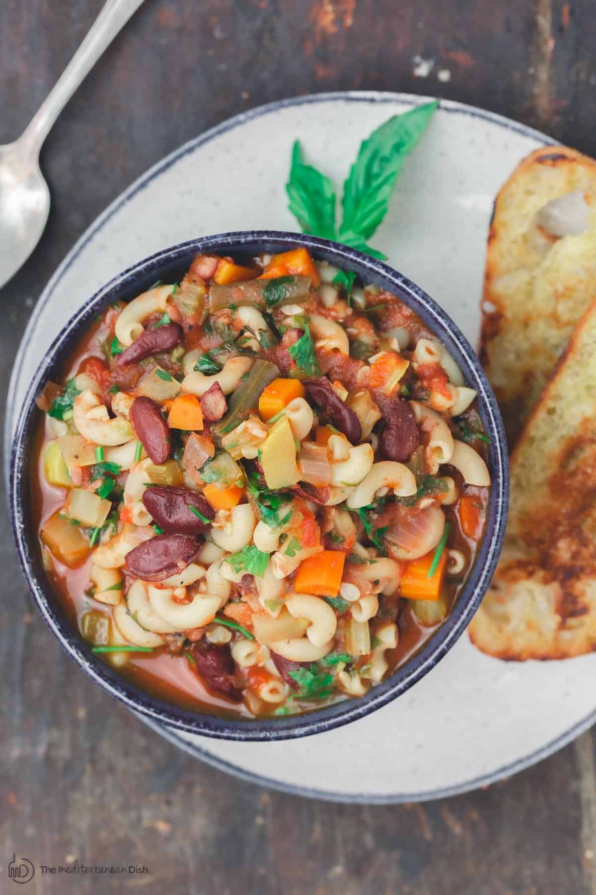 Minestrone soup in a bowl served on a plate with toast