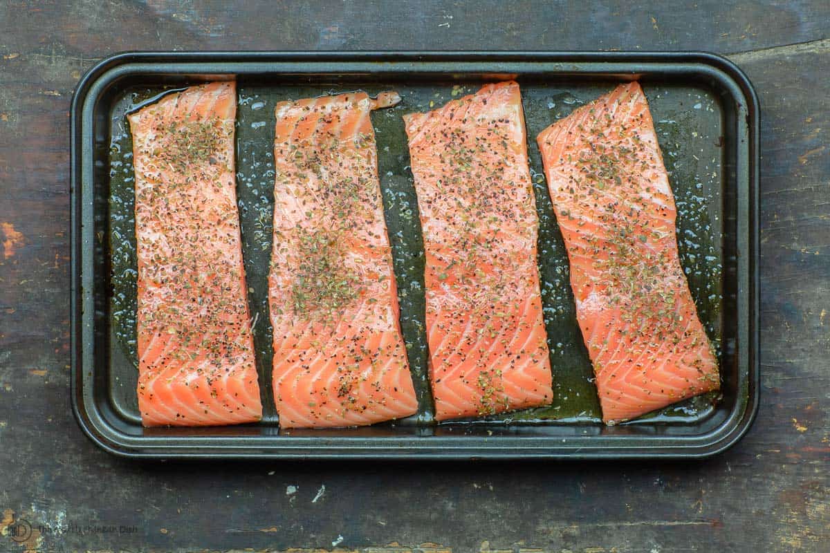 Uncooked salmon fillets seasoned in baking pan
