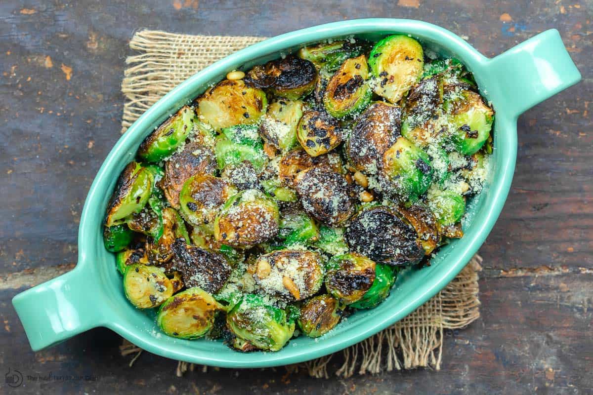 Fried brussels sprouts in serving dish with parmesan cheese and pine nuts