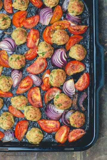 Italian baked chicken meatballs with onions and tomatoes in baking pan