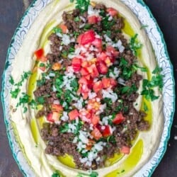 Hummus dip layered with ground beef and vegetables served in a round dish