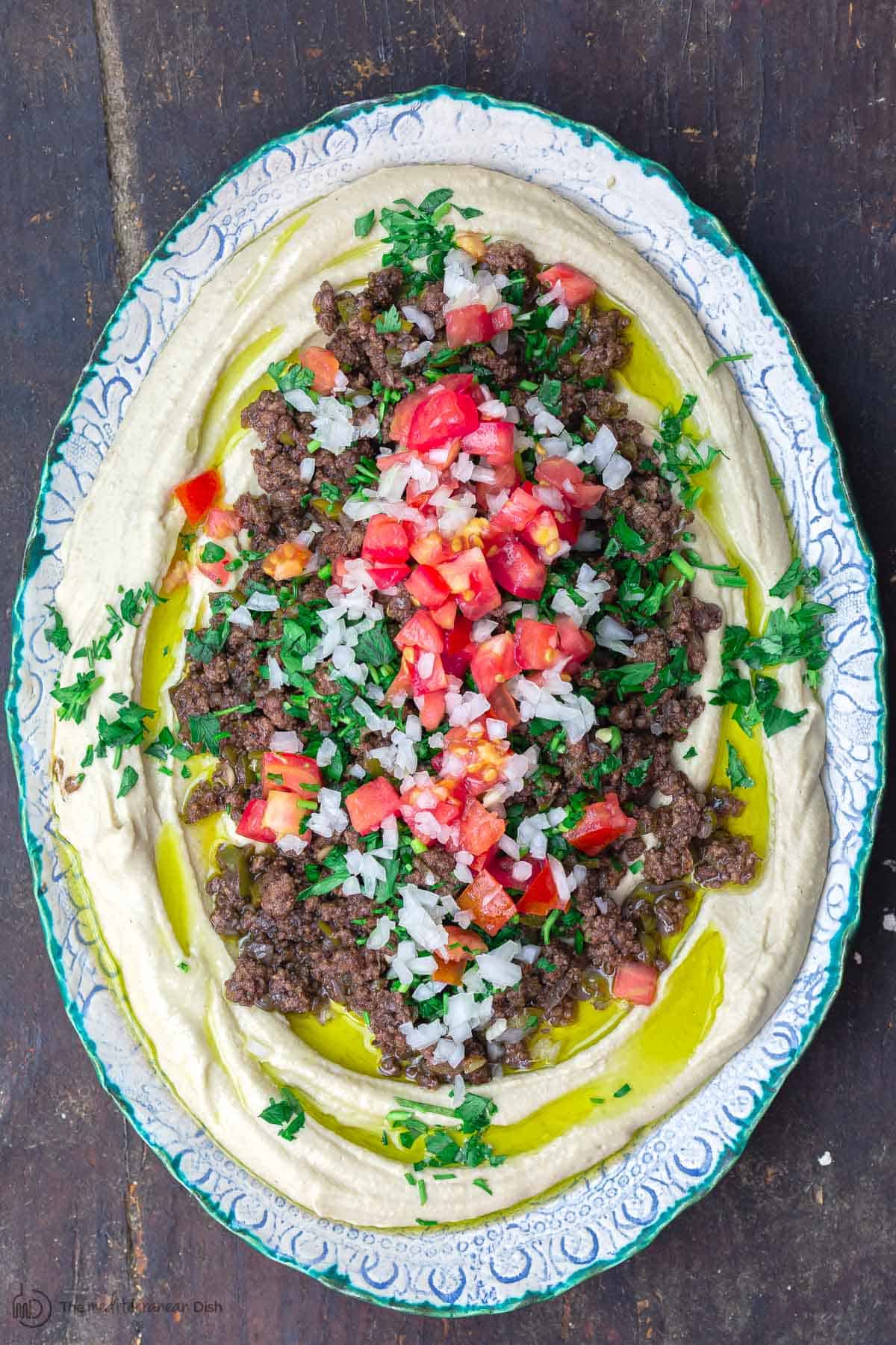 Hummus dip layered with ground beef and vegetables served in a round dish