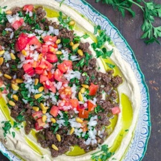 Hummus dip layered with ground beef, tomatoes, onions, parsley, and pine nuts