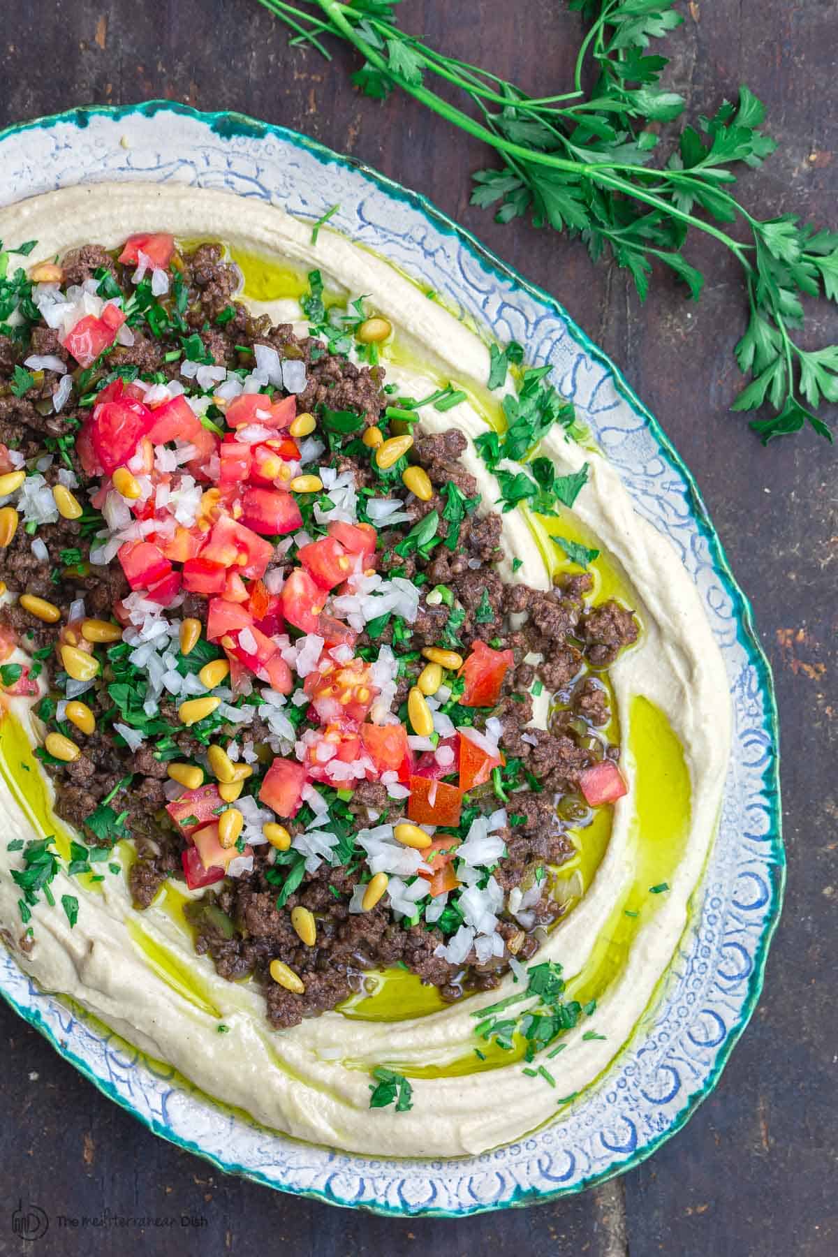 Hummus dip layered with ground beef, tomatoes, onions, parsley, and pine nuts