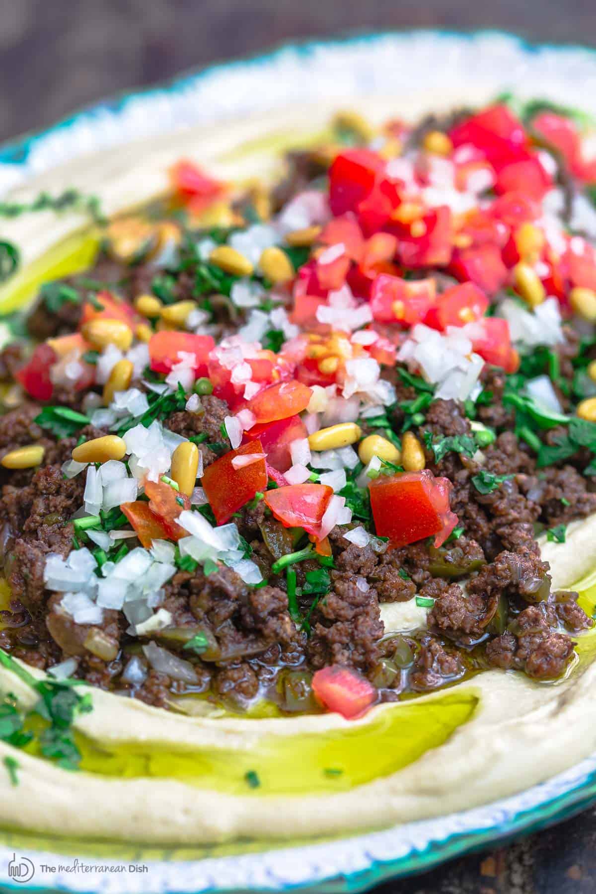 Hummus dip layered with ground beef, tomatoes, onions, parsley, and pine nuts