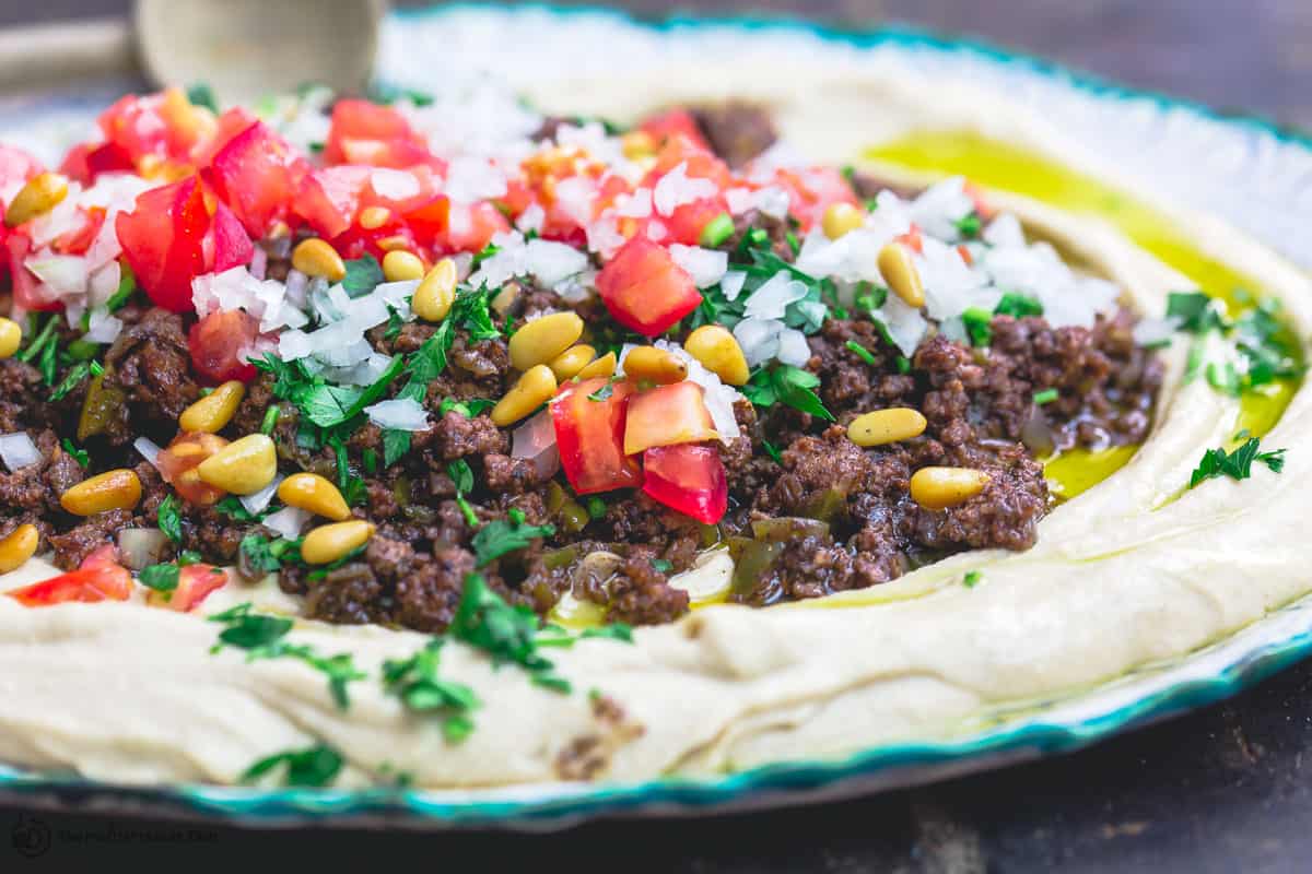 Hummus dip layered with ground beef, tomato, onions, parsley, and pine nuts