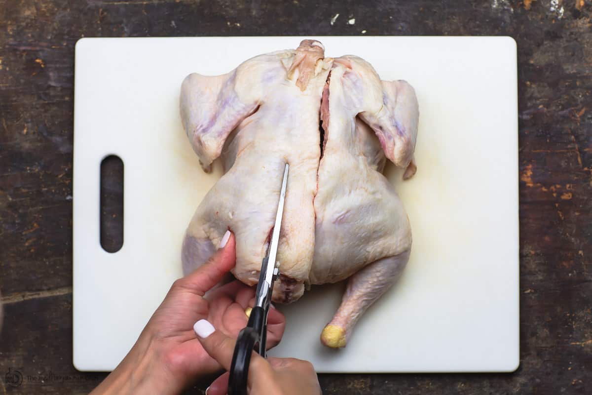 Cutting from the left side of the spine of a whole chicken